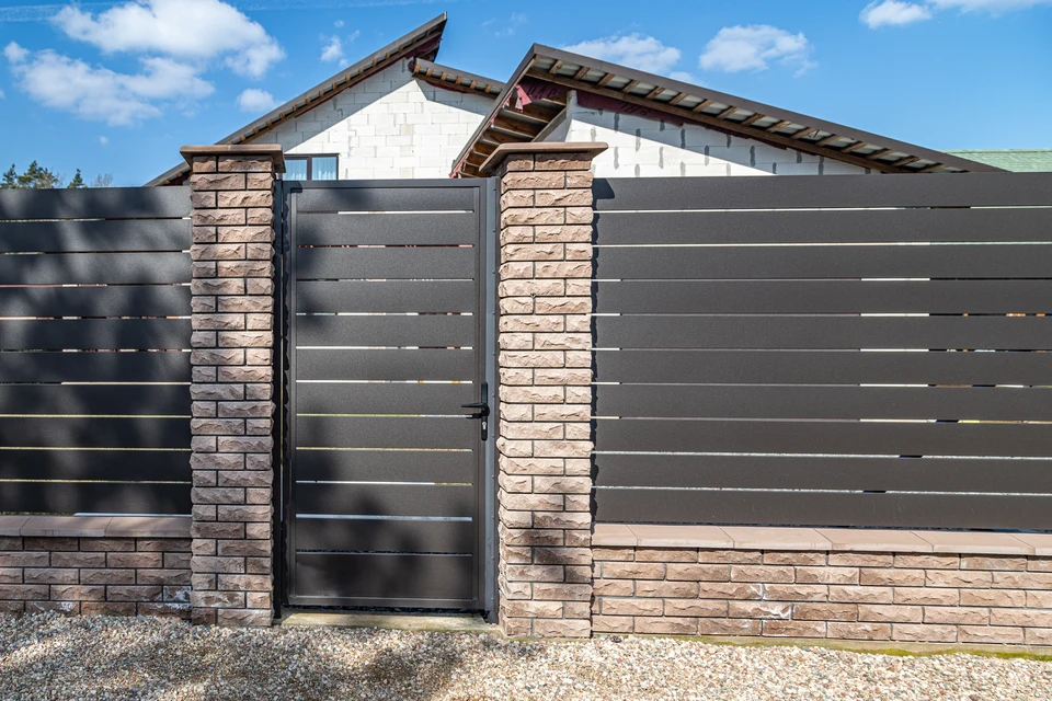 Porte de garage enroulable blanche installée sur façade en enduit blanc, encadrée de piliers en pierre calcaire taillée