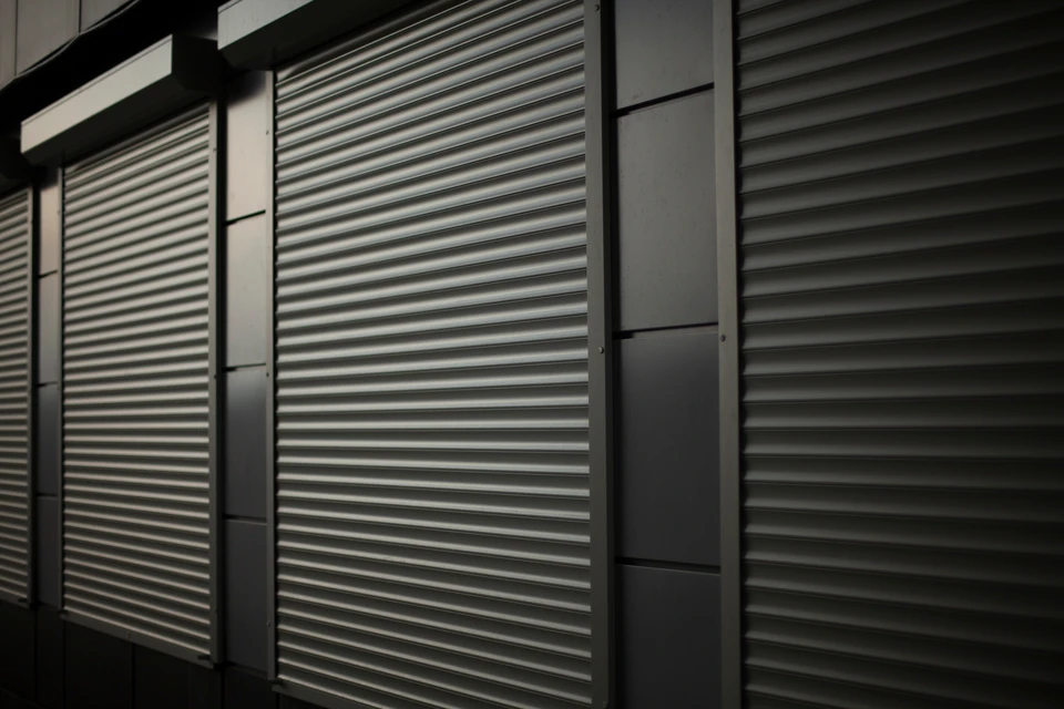 Porte de garage enroulable blanche installée sur façade en enduit blanc, encadrée de piliers en pierre calcaire taillée